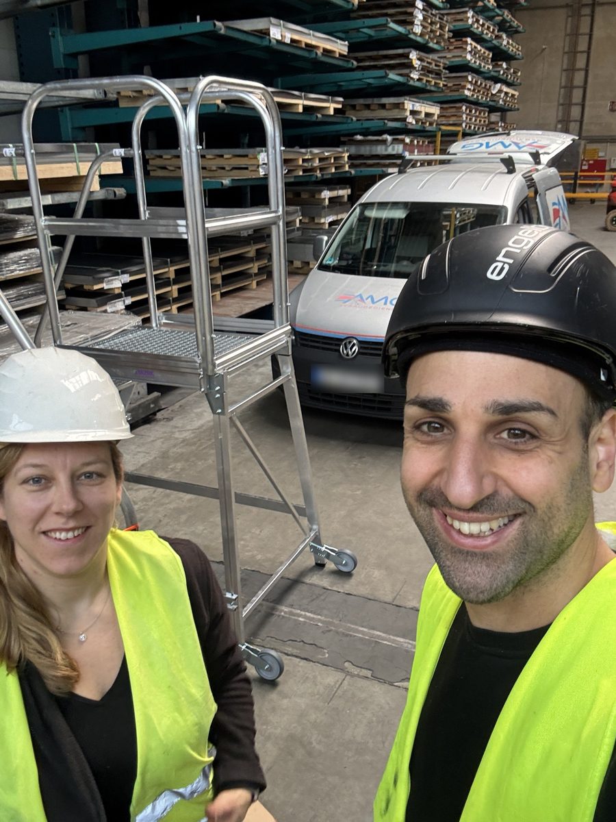 Zwei Mitarbeitende von AMG in Warnweste und Helm vor dem Firmenwagen